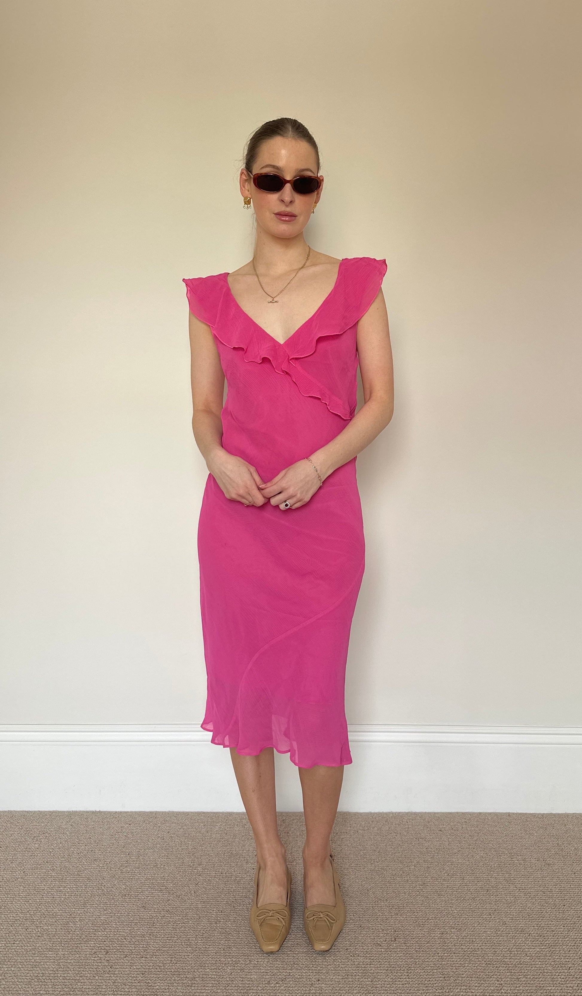 Woman wearing a pink dress against a plain wall.